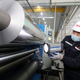 Workers examine a roll of aluminum sheet
